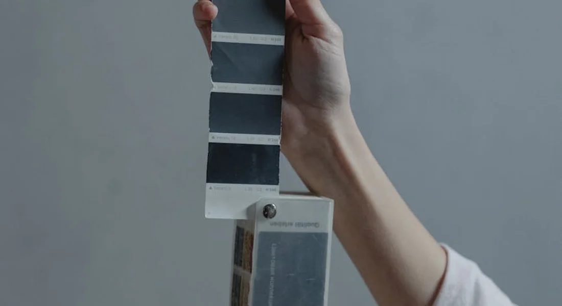 A hand holds a fan of automotive paint color swatches against a neutral background.