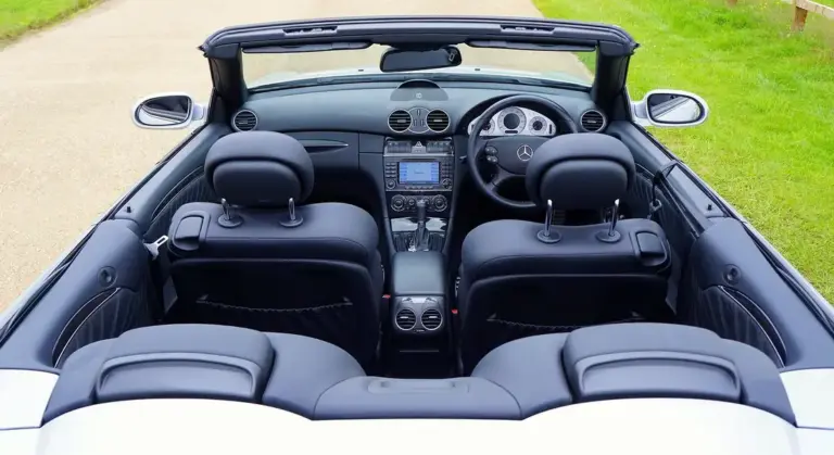 Rear-to-front view of a black leather convertible car interior, showing two front seats, center console, and dashboard outdoors.