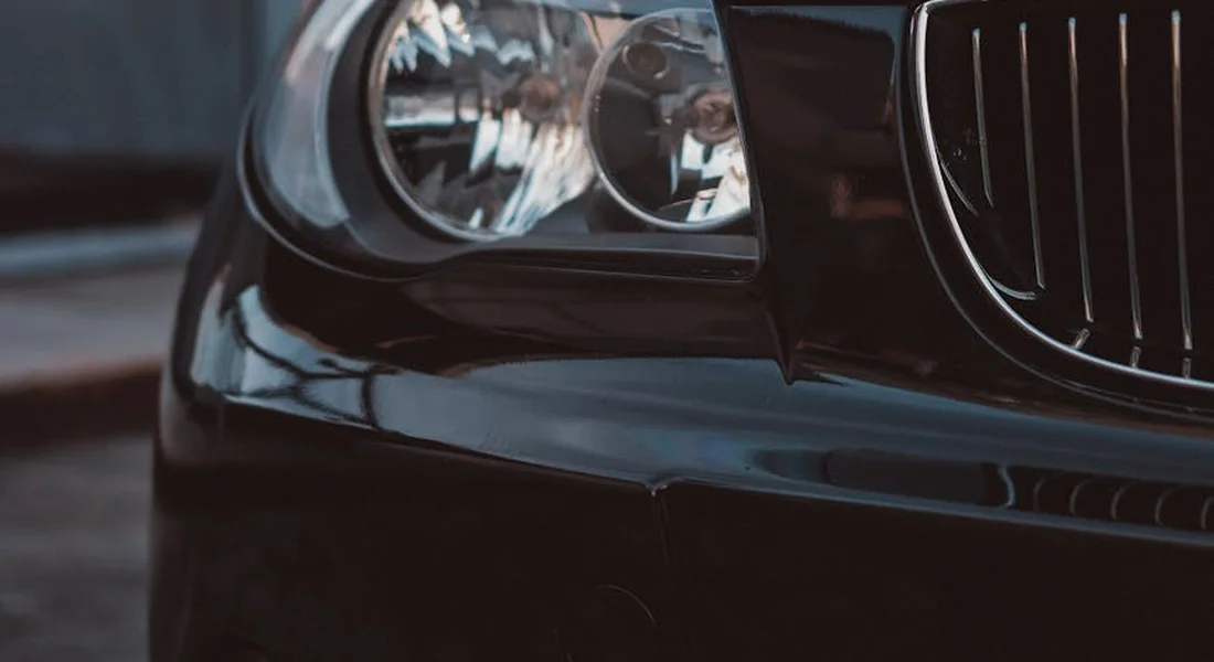Close-up of a car bumper and headlight, showing glossy black paint and reflections to aid precise scratch touch-ups.