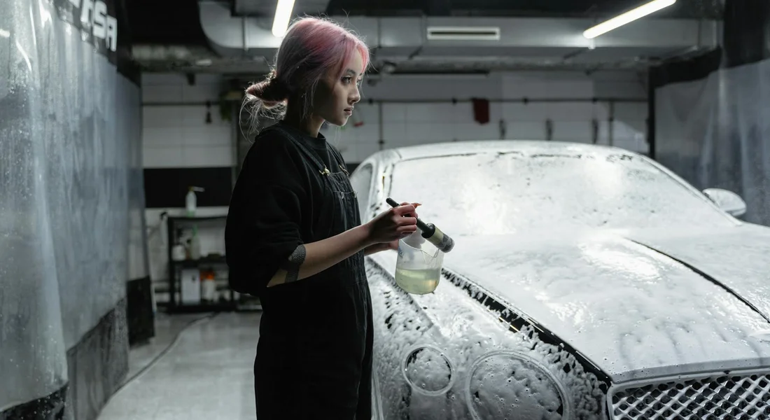 Professional car detailer in a workshop applying cleaning solution to a car.
