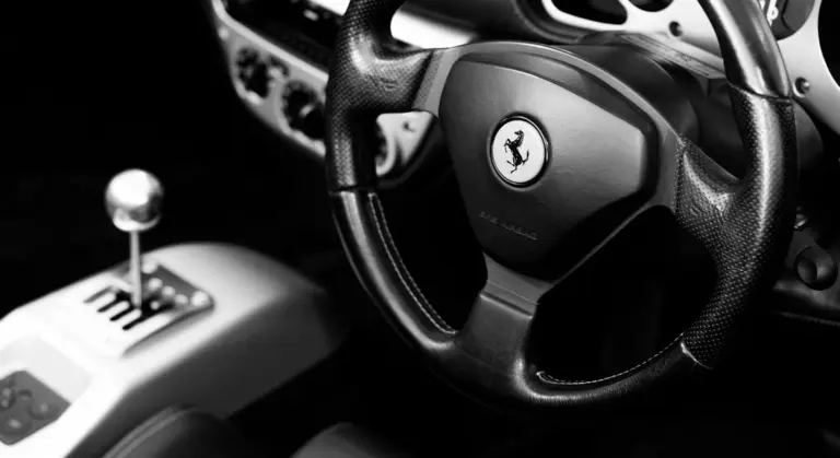 Close-up of a car interior focusing on the steering wheel with a Ferrari logo.