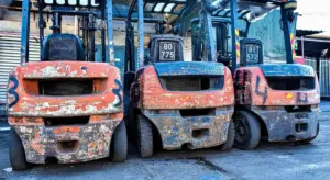 Three forklifts with chipped orange and blue paint parked side by side in a dusty lot, showing weathered finishes and scratches.
