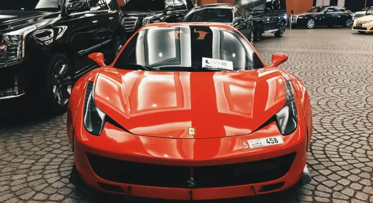 Front view of a bright red Ferrari sports car parked on a cobblestone driveway with other cars in the background.