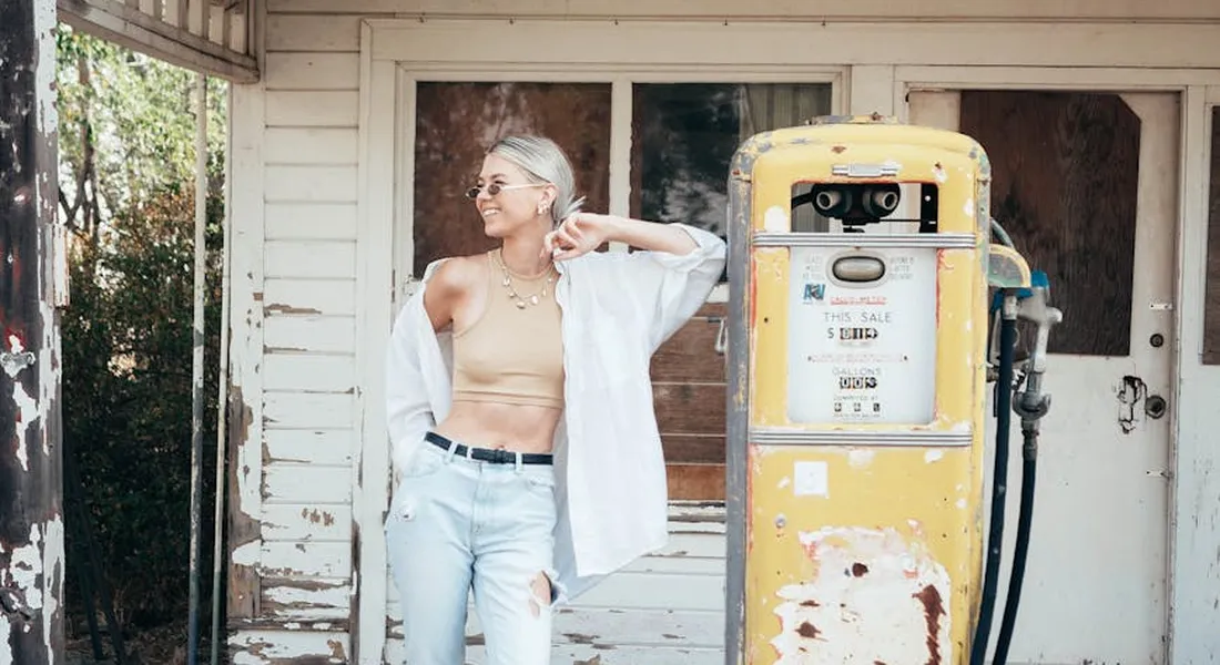 A person stands beside a vintage yellow gas pump outside a weathered wooden building, illustrating gasoline exposure scenarios for automotive paint protection.