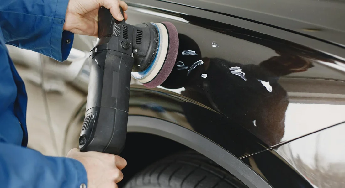 Person using a random orbit polisher on a glossy car fender, applying wax to the paint.