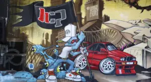 Colorful graffiti mural featuring a cartoon character spraying paint toward a red sports car.