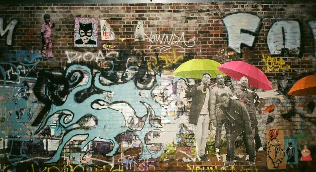 Colorful graffiti mural on a brick wall featuring abstract shapes, cartoon characters, and colorful umbrellas.