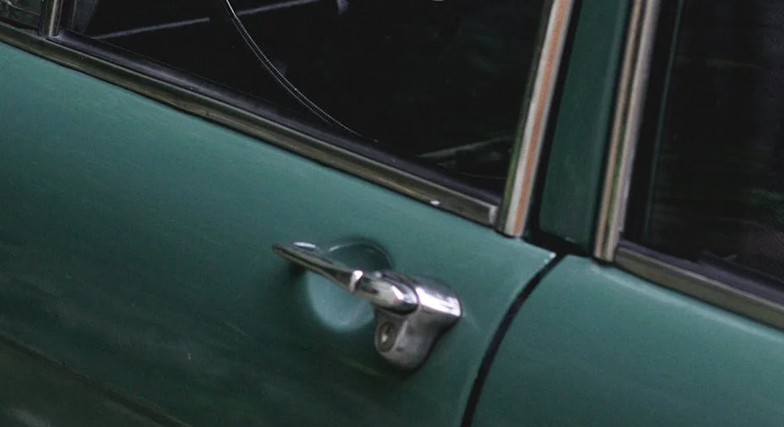 Close-up of a green car door with a chrome door handle and window frame