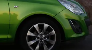 Close-up of a bright green car showing a glossy paint finish with a visible wheel and sunlight reflections.