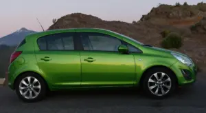 Side view of a bright green hatchback car parked on a road with desert hills in the background.