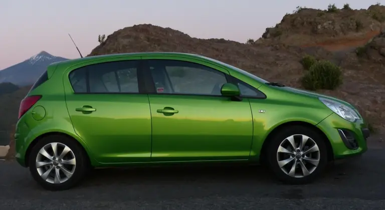 Side view of a bright green hatchback car parked on a road with desert hills in the background.