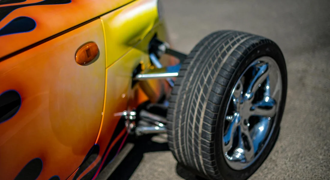 Close-up of an orange car body with a visible wheel and a floor jack, illustrating DIY auto painting prep.