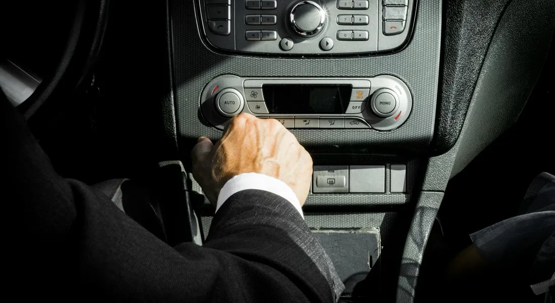 Close-up view of a vehicle's center console with a person in a suit reaching toward the gear area.