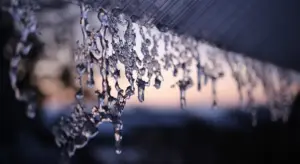 Icicles hanging from the edge of a car in winter, with a blurred background.