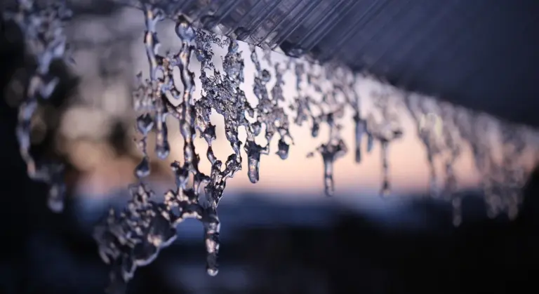 Icicles hanging from the edge of a car in winter, with a blurred background.