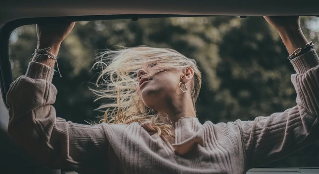 Person sitting in a car with the window open, wind blowing their hair.