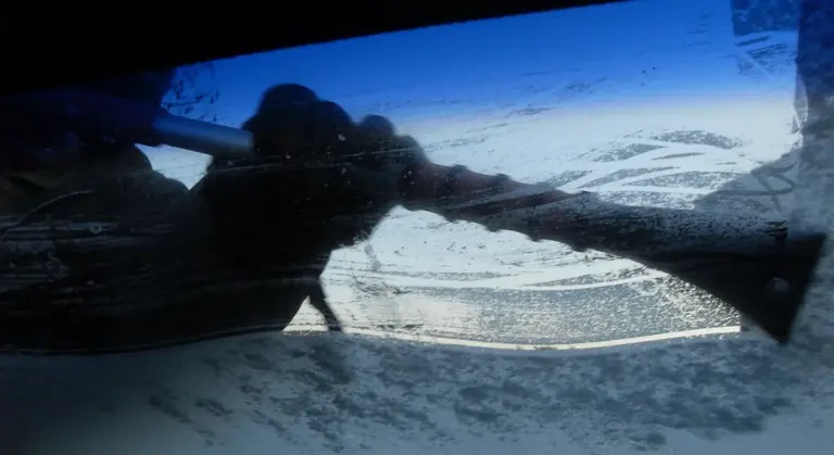 Inside of a car with a person cleaning the interior windshield using a squeegee or cloth.