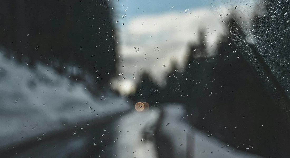 Inside view of a car windshield with water droplets on the glass and a snowy street outside, creating a blurred, streaky look