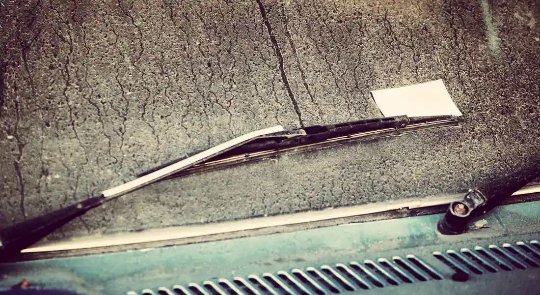 Close-up of a car's windshield with a wiper blade resting at the base, highlighting possible interior smudges and dust buildup.