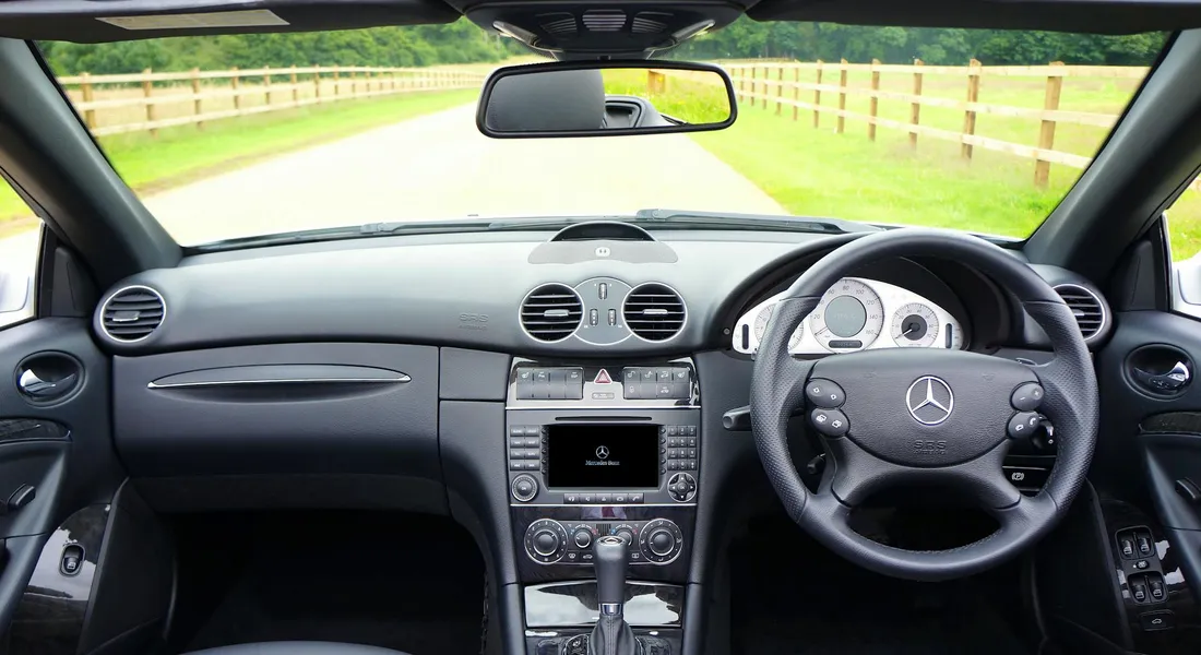 Interior view of a Mercedes-Benz showing the steering wheel, center console, and dashboard with a clear road view through the windshield.