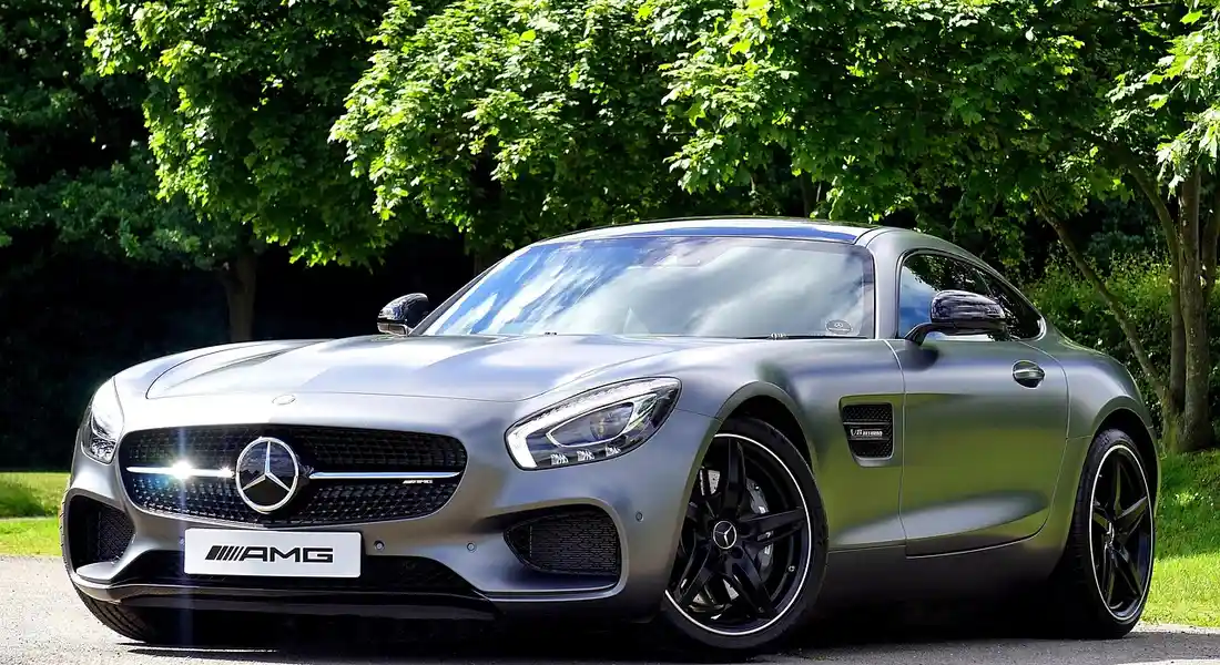 Grey Mercedes-Benz AMG roadster with a glossy, reflective paint finish parked outdoors among green trees.