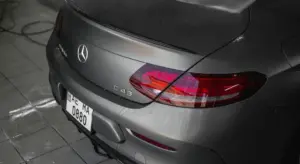 Rear view of a gray Mercedes-Benz C43 AMG in a garage, showing the trunk lid, taillights, and a visible license plate.