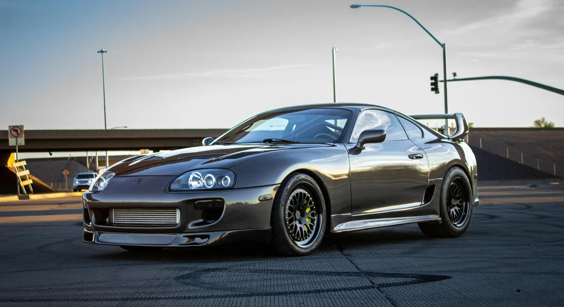 Gray modified sports car with a large rear spoiler parked in an outdoor lot on a sunny day.