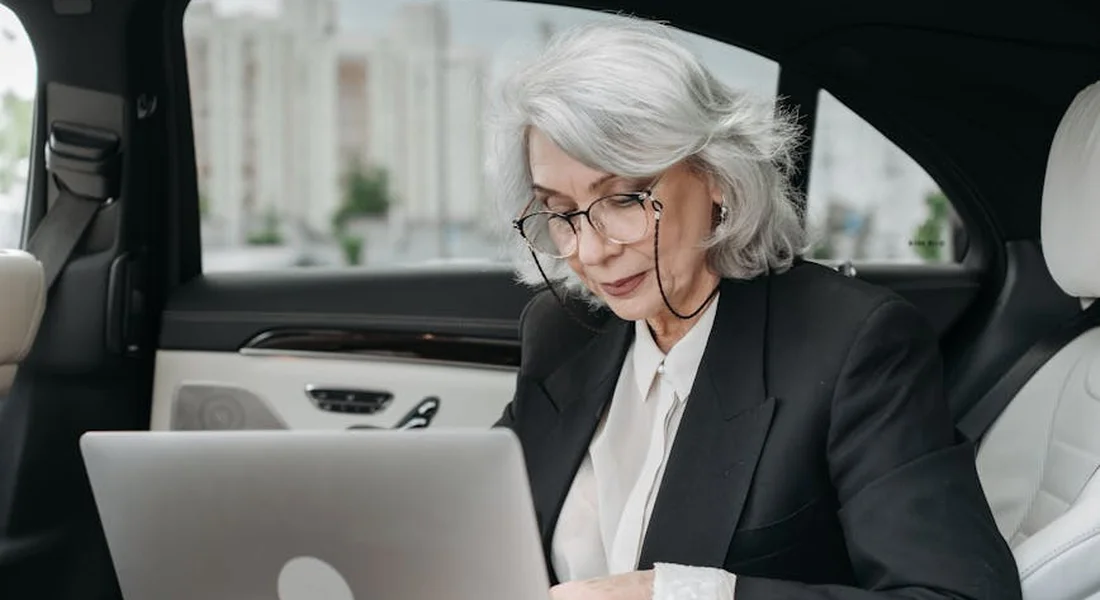 Professional woman in a blazer sits in a car interior using a laptop, researching mold removal products.