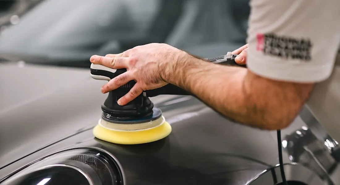 Person using a polishing tool on the hood of a freshly painted car