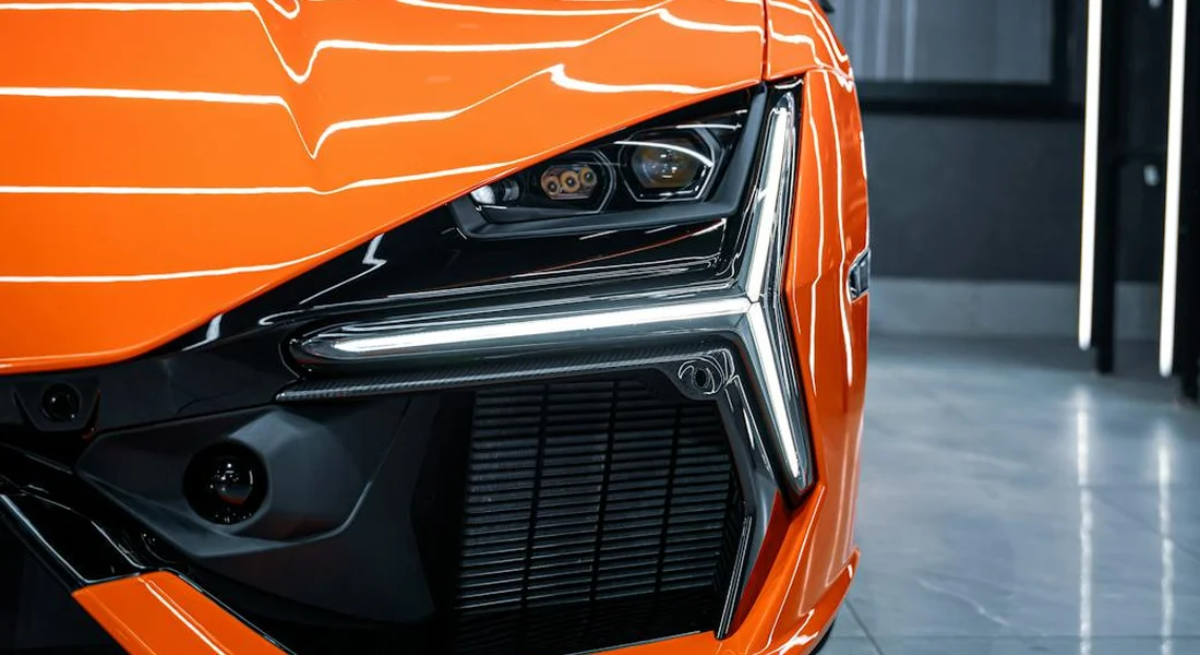 Close-up of a bright orange car's front end, featuring a glossy finish and modern headlight.