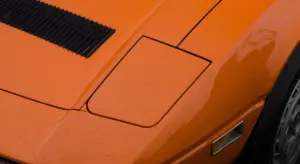 Close-up of an orange car hood with water droplets and panel lines, showing a glossy coated surface.