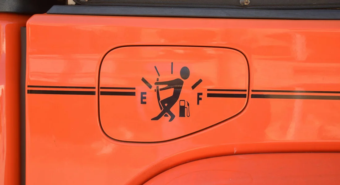 Close-up of an orange panel with a black outlined fuel gauge graphic and a stylized figure cleaning.