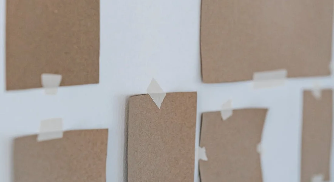 Wall with several brown tape sample patches secured by small pieces of masking tape, illustrating tape testing for paint protection.
