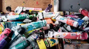 A chaotic pile of colorful artist paint tubes in a studio, representing color matching for car touch-ups