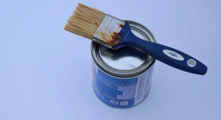 Blue paint can with a brush resting on top against a light blue background.