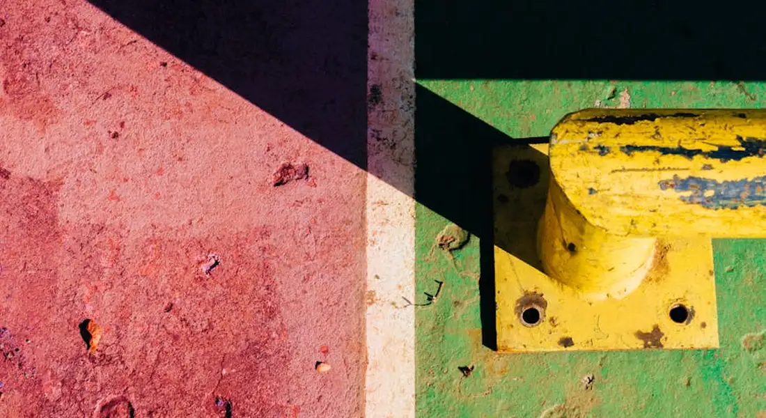 Close-up of a car-painted surface with red and green sections showing paint chips and wear, including a yellow component.