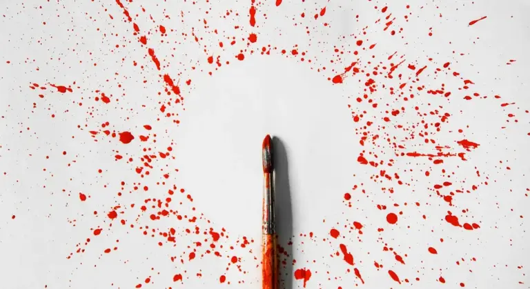 Red paint splatters around a central paintbrush tip on a white background, illustrating blending and layering in automotive paintwork.