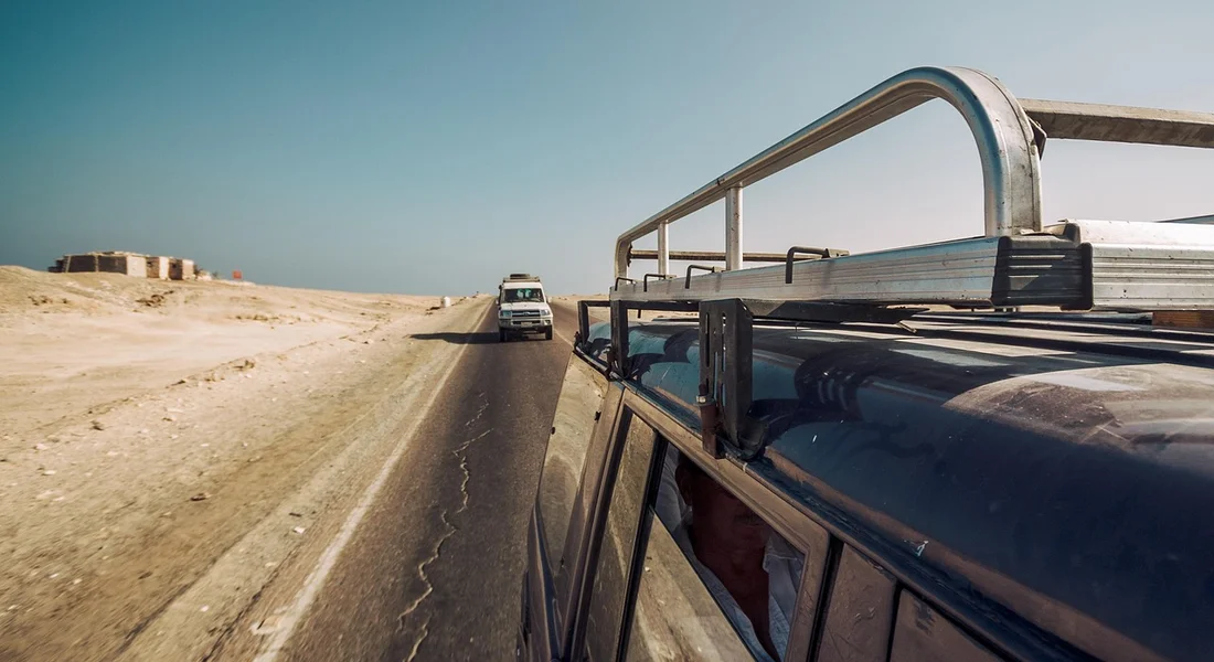 Side view of a vehicle on a desert highway with a roof rack, illustrating the transition from flat roof panels to curved bumper areas in vinyl wrapping.