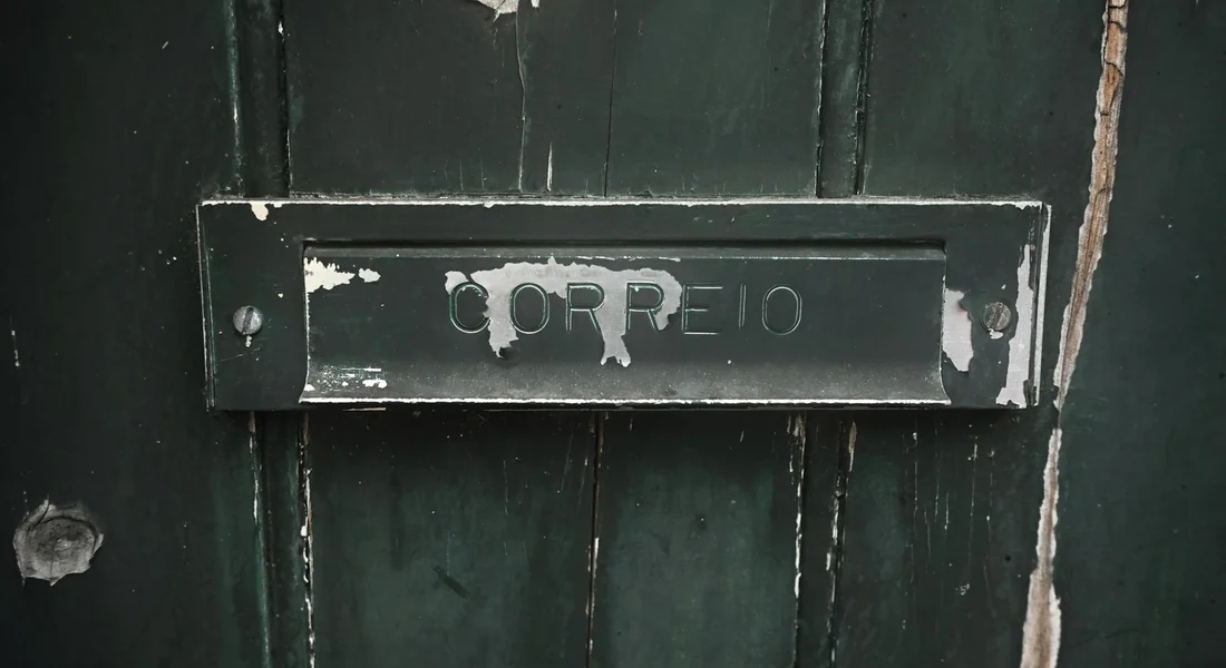 Dark green wooden door with a weathered metal mail slot; chipped paint around the slot, illustrating peeling surfaces similar to peeling car paint.