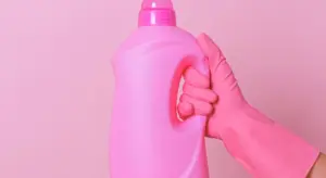 Pink cleaning bottle held by a gloved hand against a pink background, suggesting gentle, non-abrasive cleaning for car plastic trim