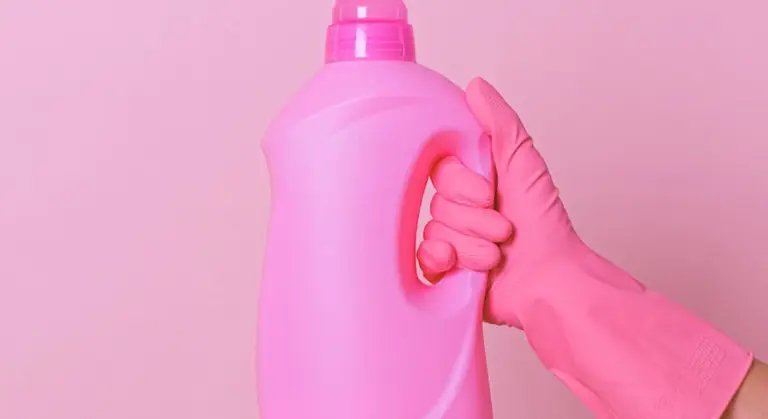 Pink cleaning bottle held by a gloved hand against a pink background, suggesting gentle, non-abrasive cleaning for car plastic trim