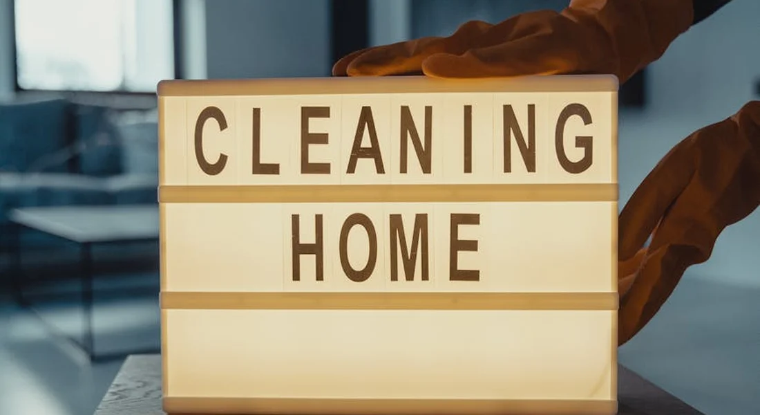 Gloved hands adjust a lightbox sign that reads 'CLEANING HOME', symbolizing readiness and cleanliness before steam cleaning.