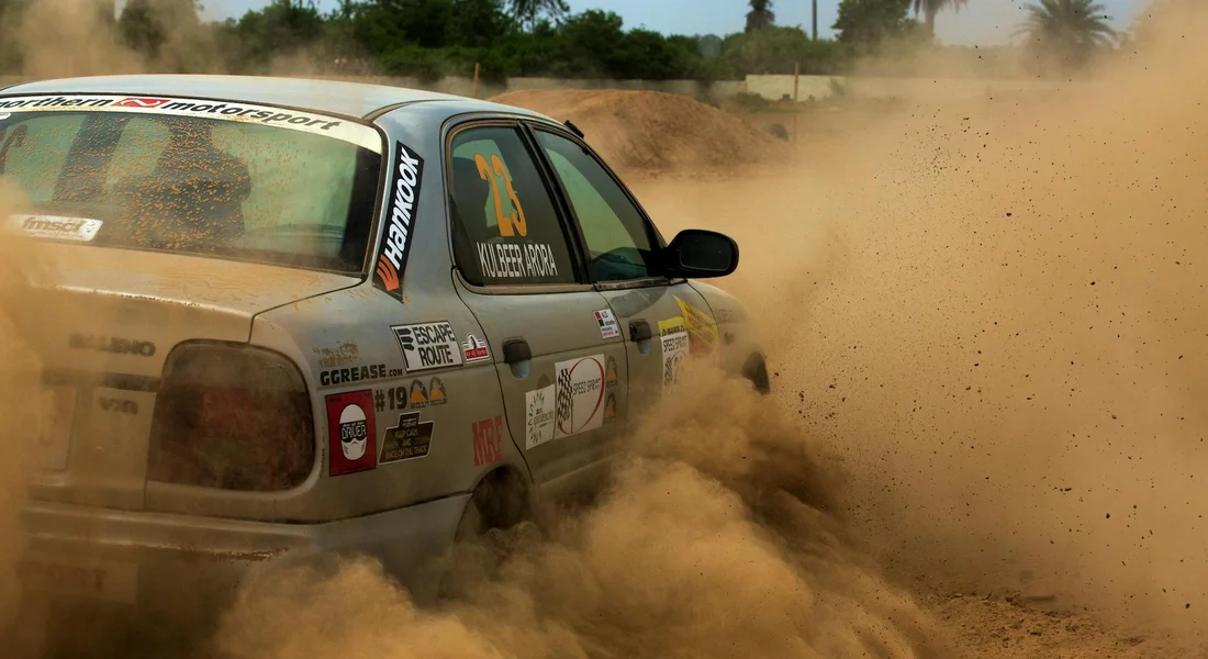 Dusty rally car on a dirt track kicking up a large cloud of dust as it speeds by.