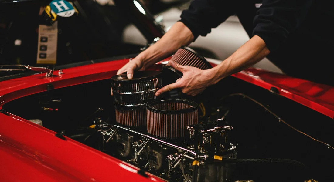 Hands installing air filters in the engine bay of a red car.