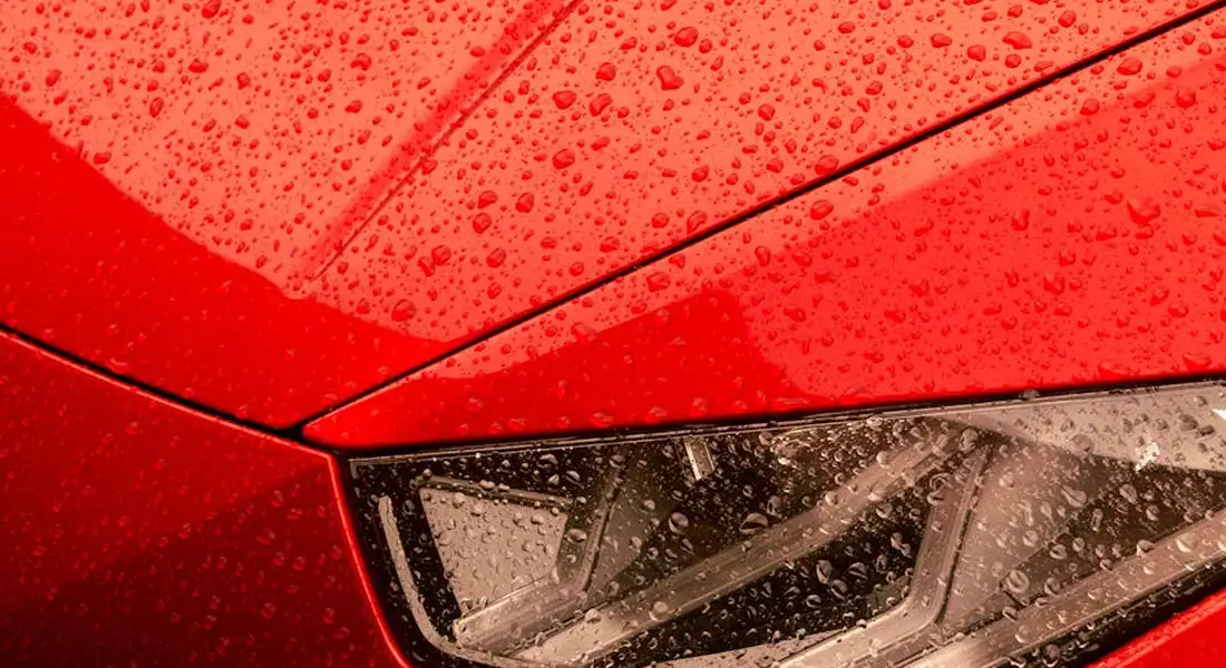 Close-up of a red car's glossy paint with water droplets and a portion of the headlight