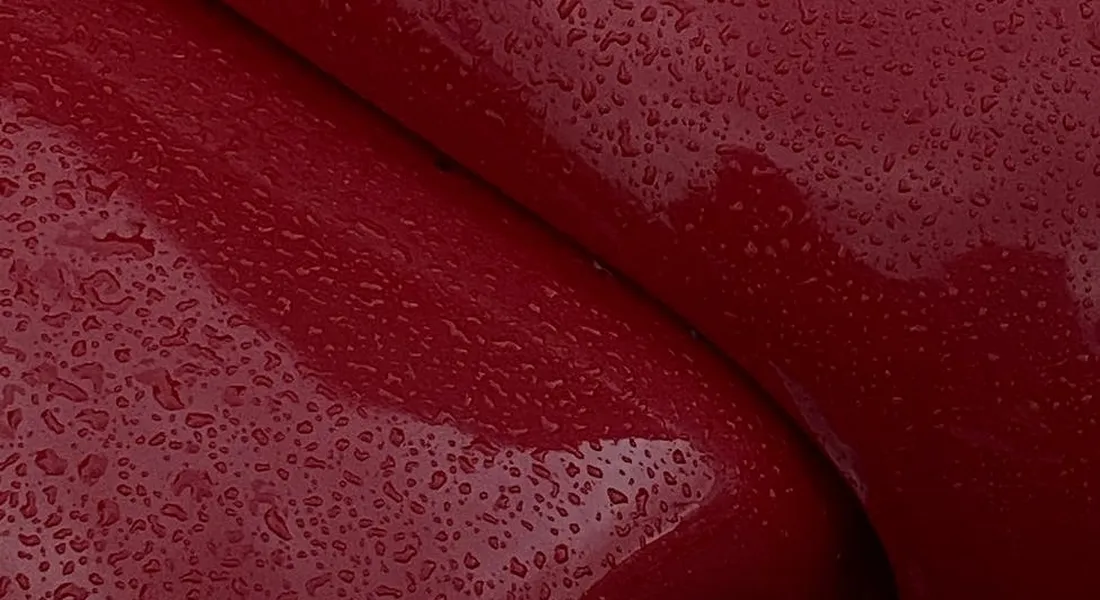 Close-up of glossy red car paint with water droplets beading on the surface