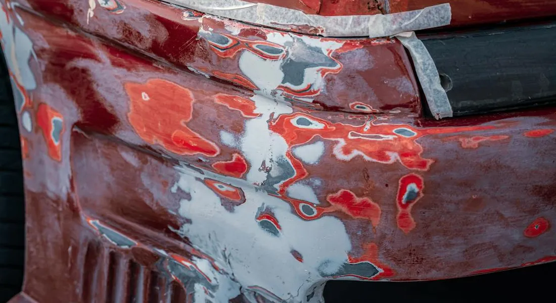 Close-up of a red car bumper with a deep scratch and exposed underlying layers beneath the clear coat.
