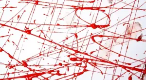 Close-up of red spray paint splatters and drips on a white surface.