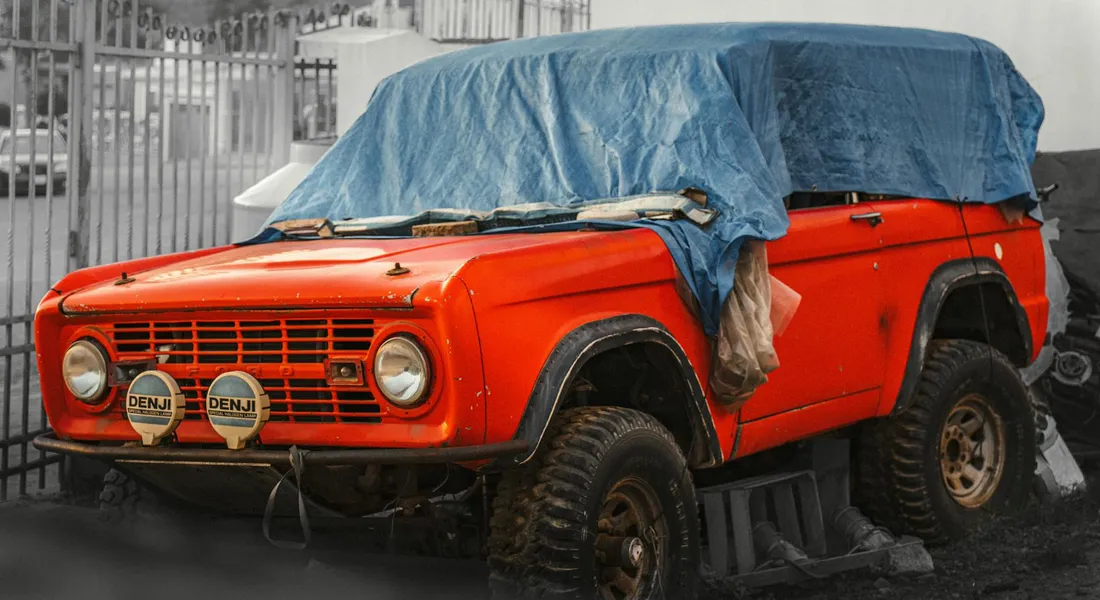 Red vintage SUV covered with a blue car cover in a driveway.