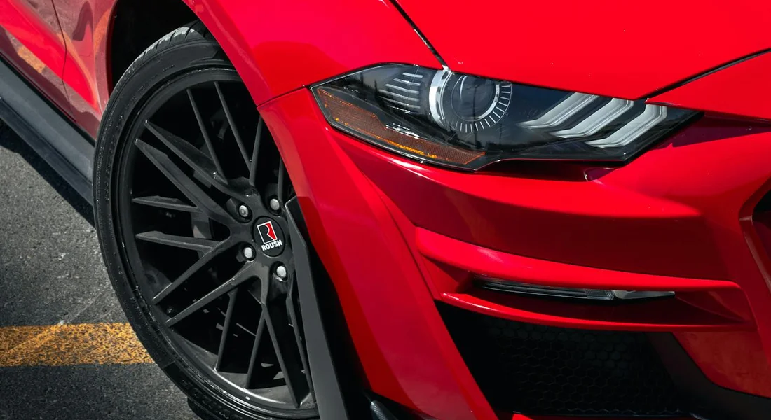 Close-up of a red sports car's front end with a black alloy wheel and headlight.